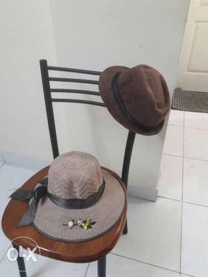 One Brown Fedora Hat With Black Band And One Gray Sun Hat